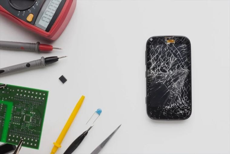 Phone repair tools and a cracked screen at a Fonedaddy repair bench